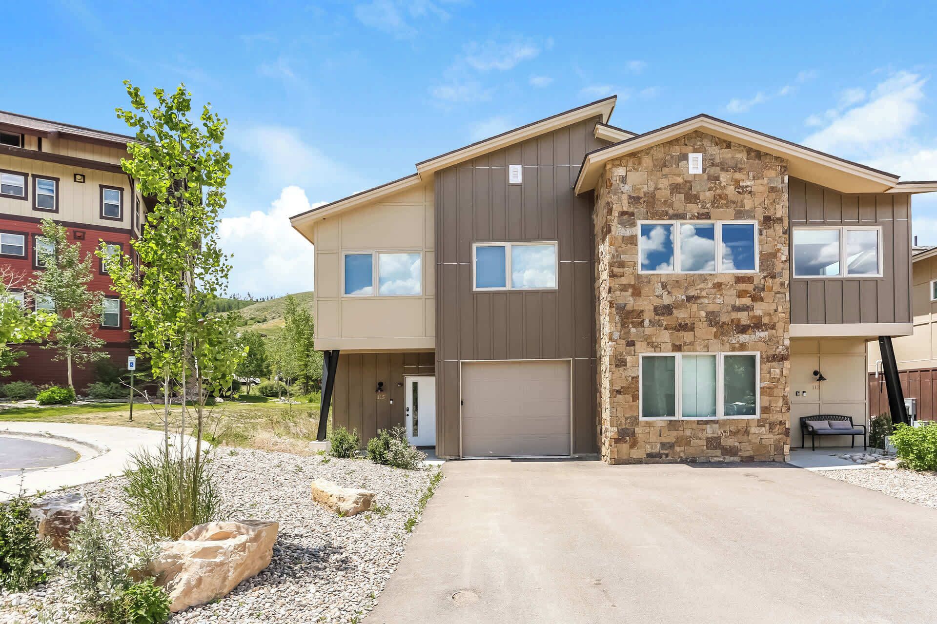 A modern two-story residential building with a stone facade, multiple windows, and a driveway.