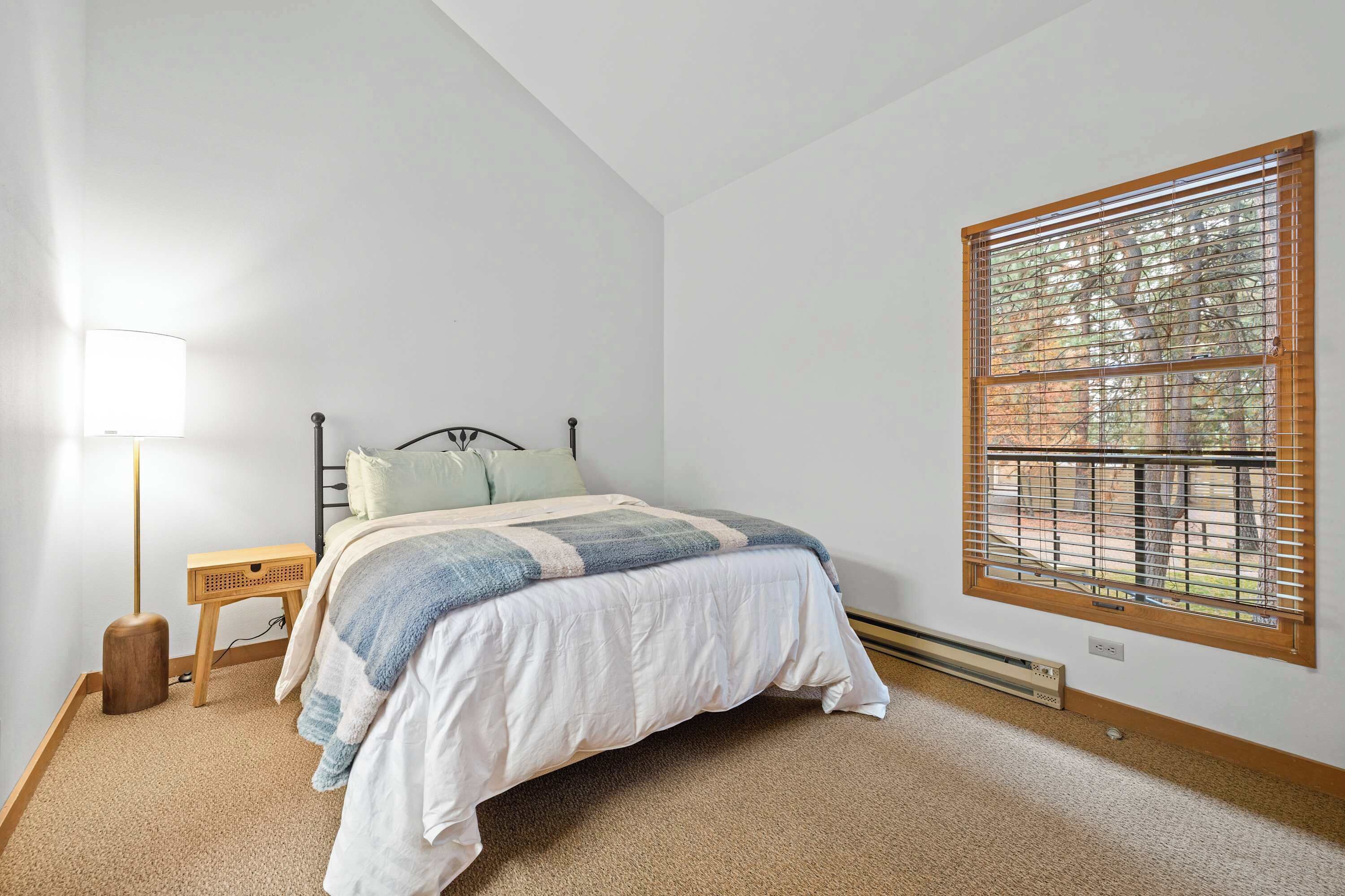 A bedroom with a bed, bedside table, lamp, and a window with blinds.