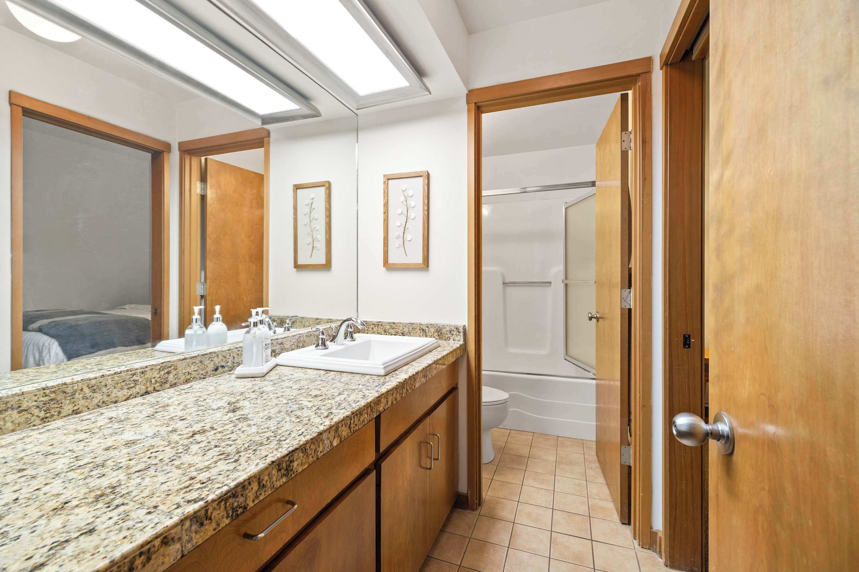 A bathroom with a granite countertop, two sinks, a toilet, and a shower.