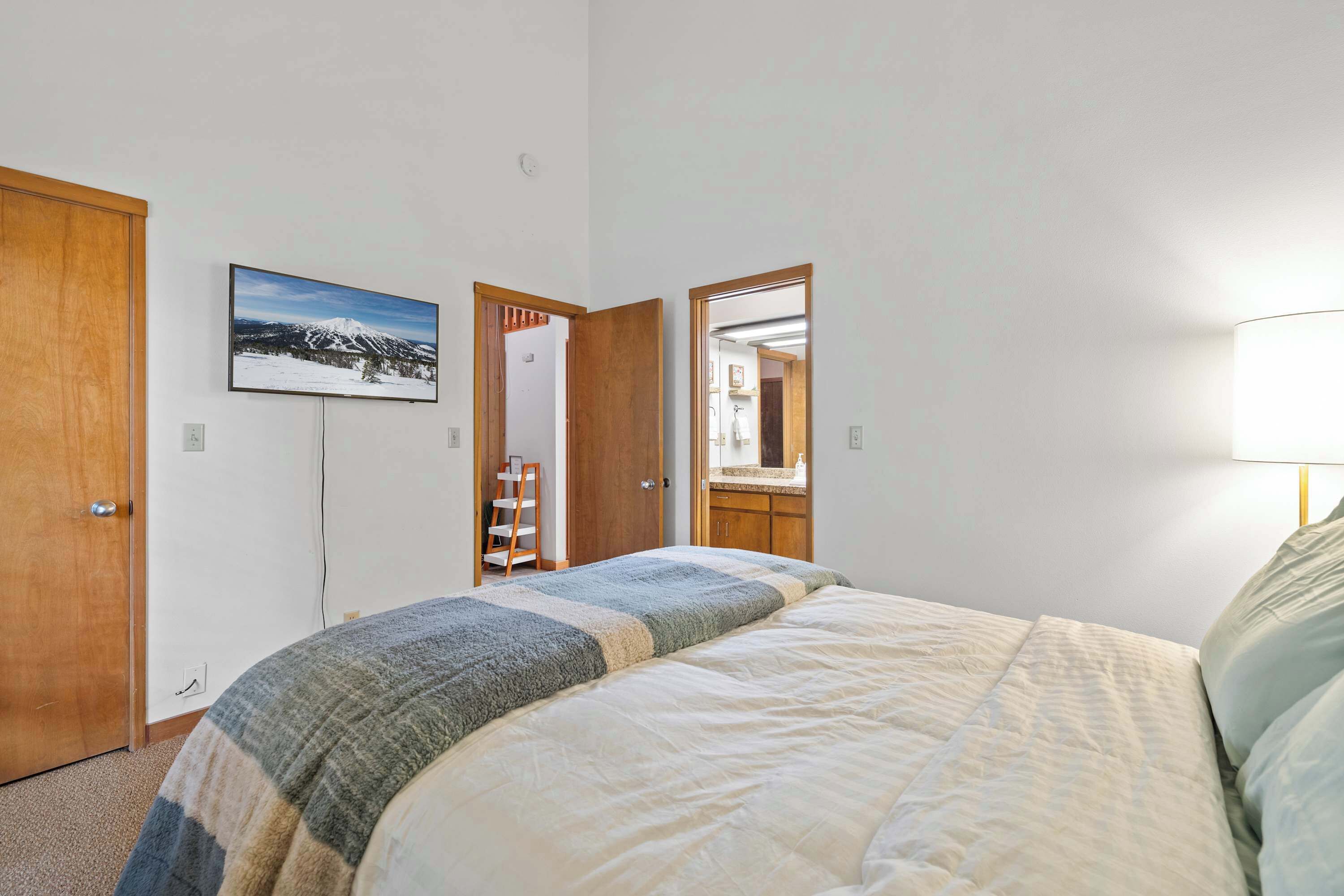 Camera da letto con un letto, una porta in legno, un quadro appeso al muro e uno specchio che riflette un bagno.