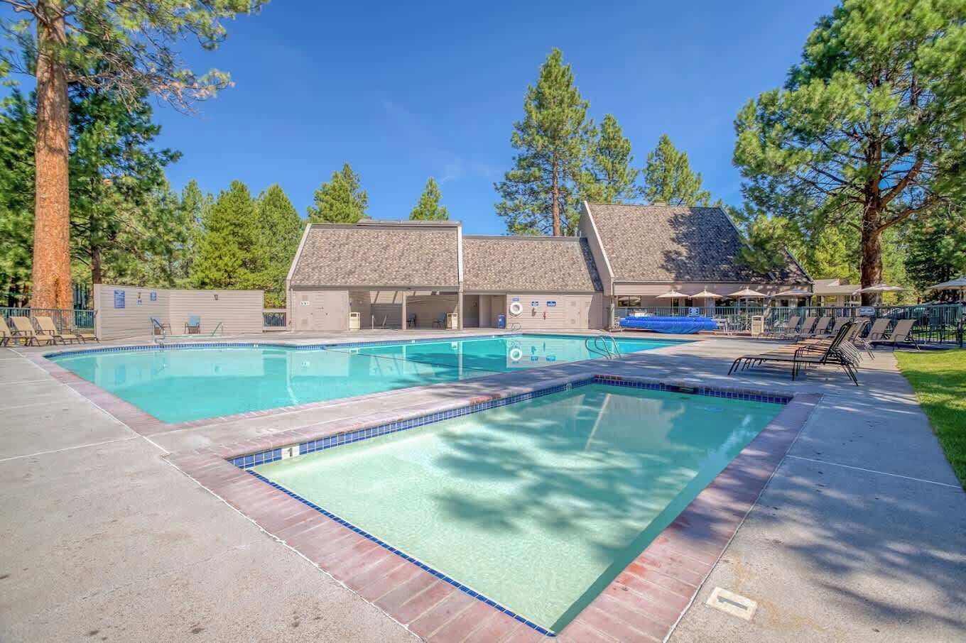 Un área de piscina con dos piscinas rectangulares, rodeada de sillas de descanso y un edificio con techo inclinado.