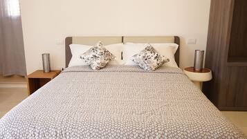 Un lit recouvert d’une couvre-lit à motifs, deux oreillers ornés de motifs floraux et deux tables de chevet surmontées de lampes cylindriques.