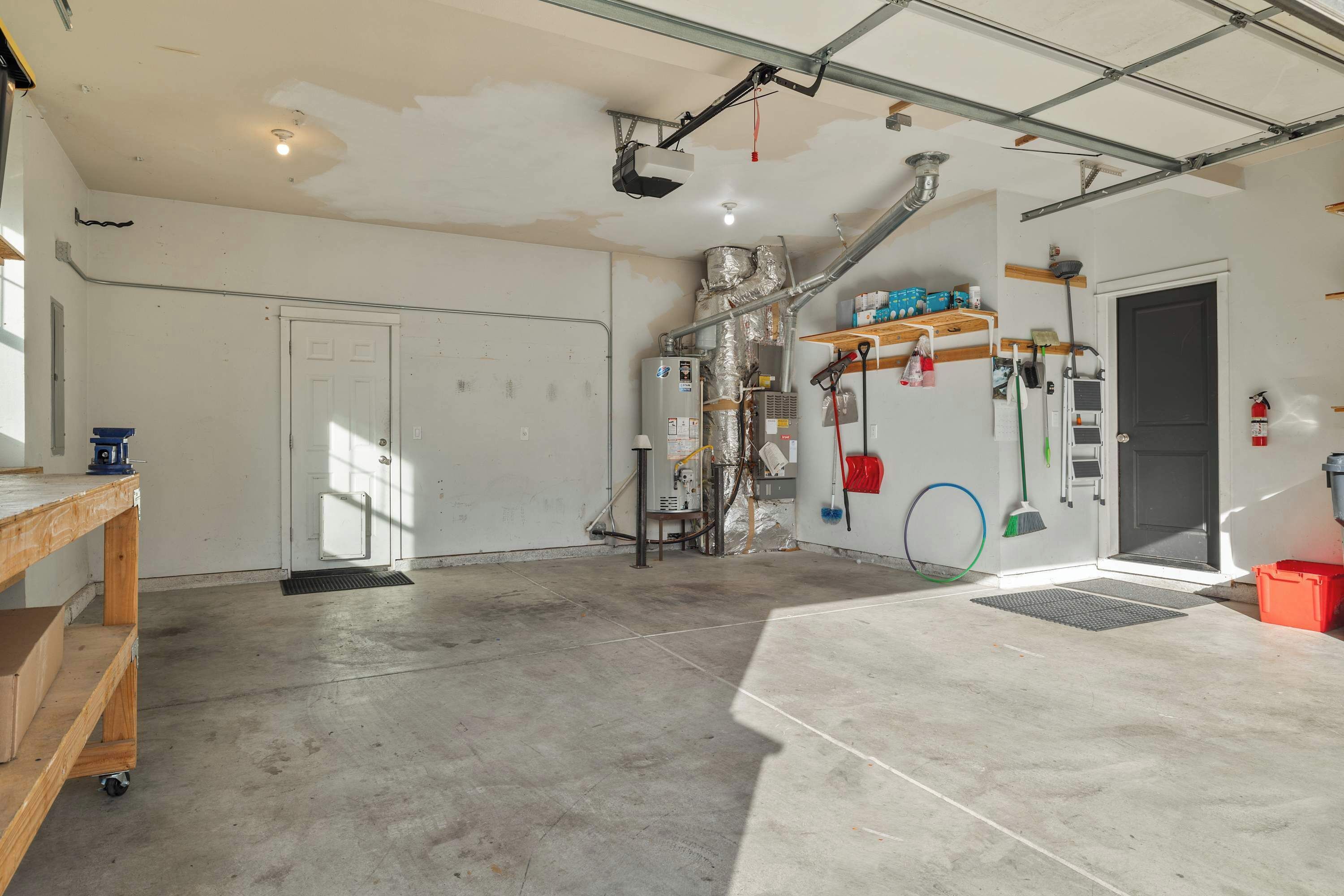 A spacious garage with a concrete floor, a white door, and a workbench.