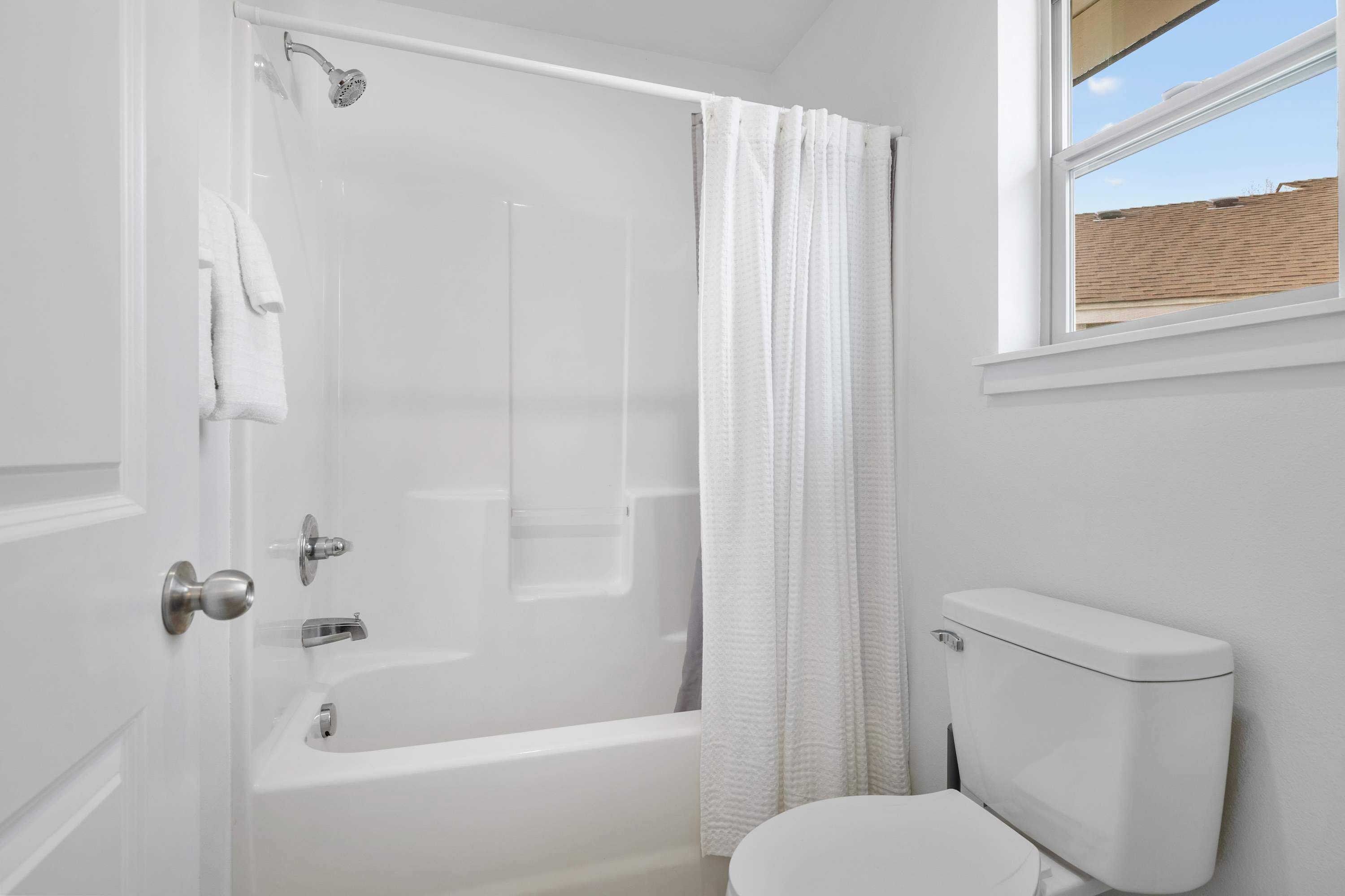 Ein Badezimmer mit Badewanne, Toilette und einem Fenster mit Blick auf eine Ziegelwand.