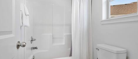 Ein Badezimmer mit Badewanne, Toilette und einem Fenster mit Blick auf eine Ziegelwand.
