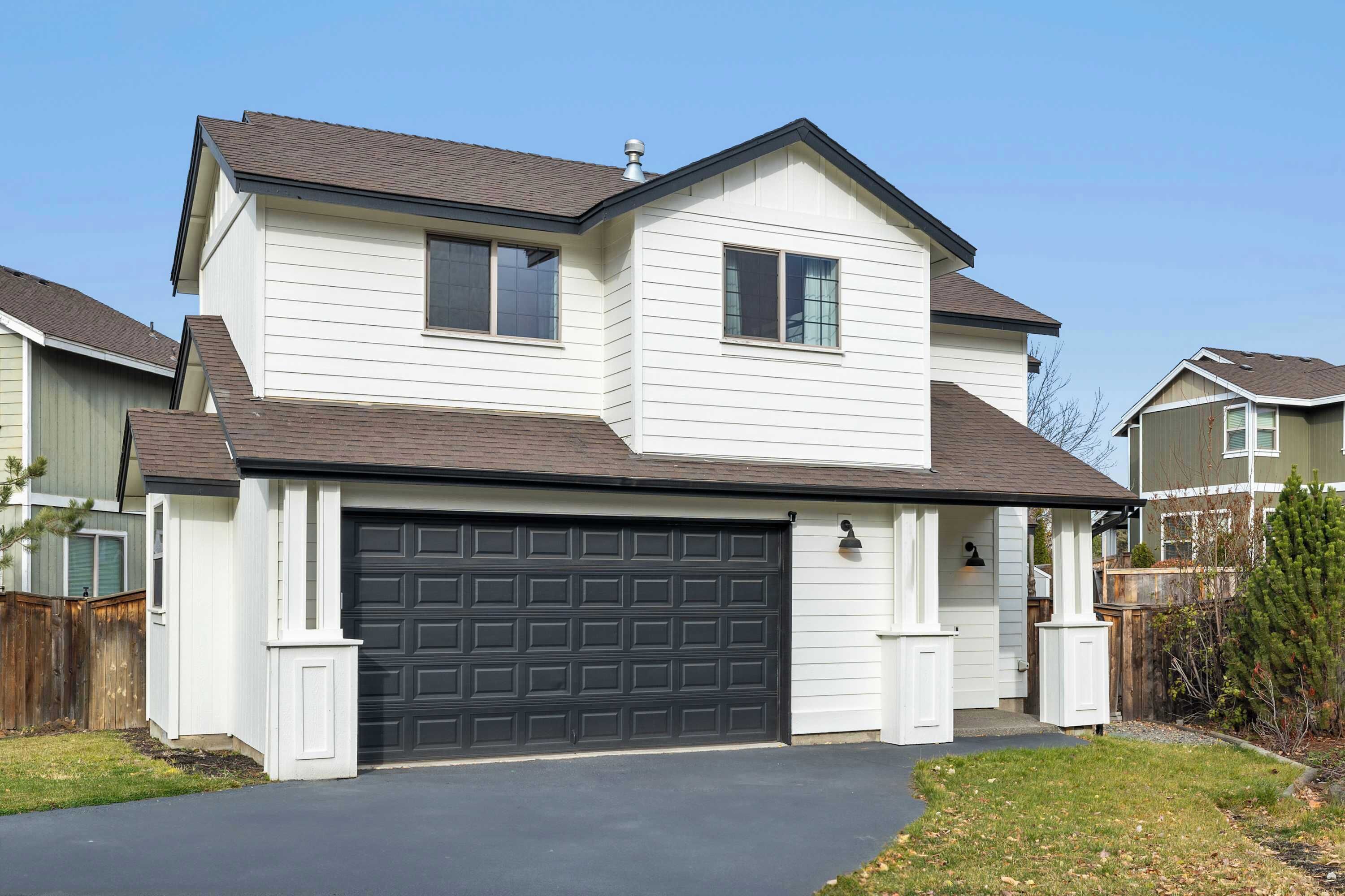 A two-story house with a dark garage door, white siding, and a sloped roof.