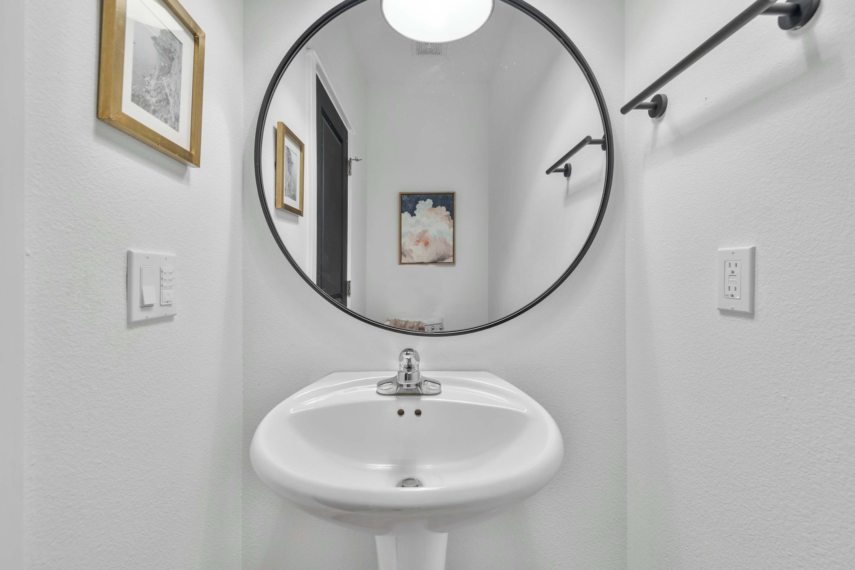 Ein Badezimmer mit einem weißen Waschbecken, einem runden Spiegel und gerahmten Bildern an den Wänden.