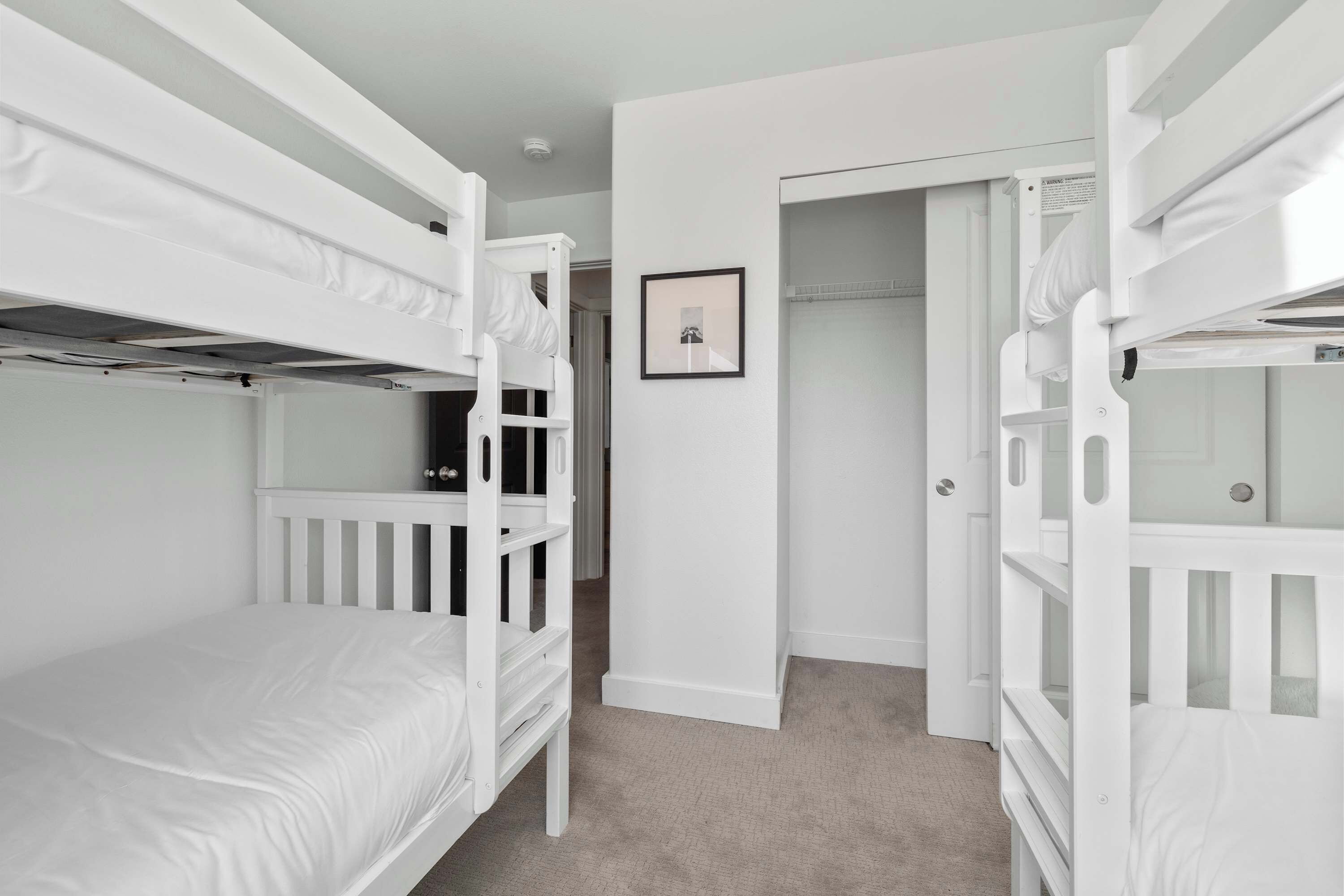 A room with bunk beds, a framed picture on the wall, and a door leading to another room.