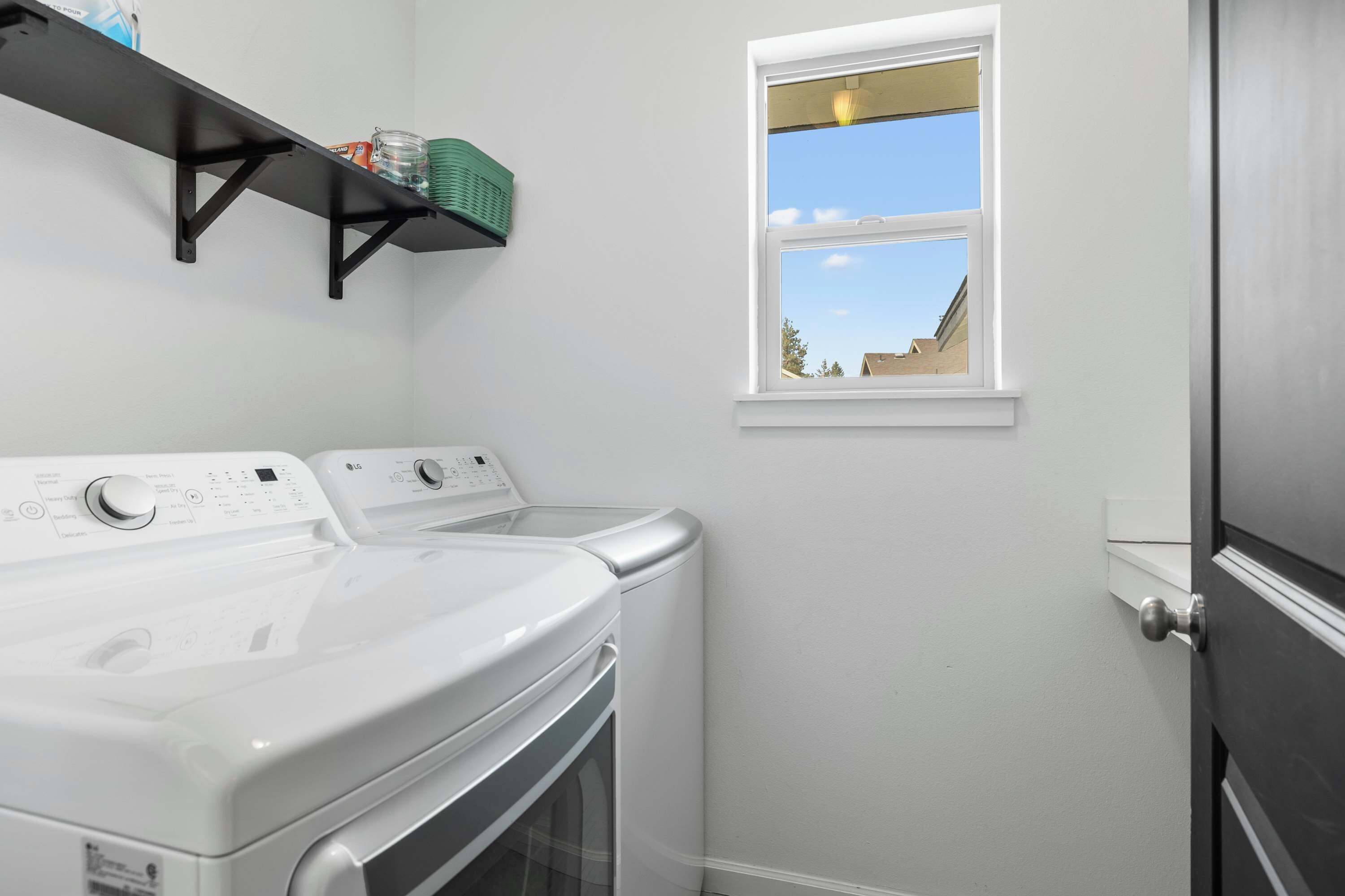 A laundry room with a white washing machine and dryer, a shelf with laundry supplies, and a window with a view of the outside.