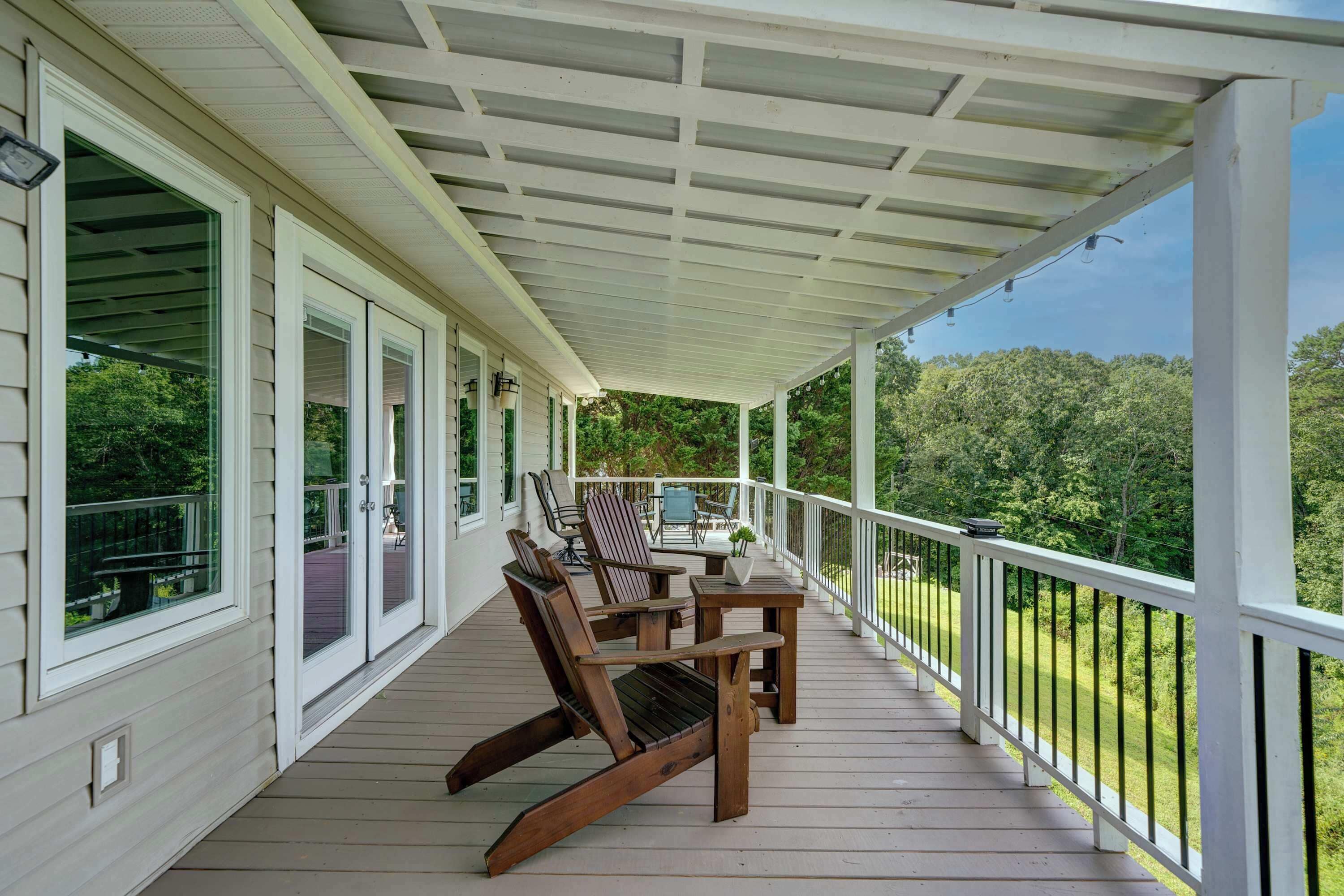 A covered porch with wooden chairs and a table, overlooking a green landscape.