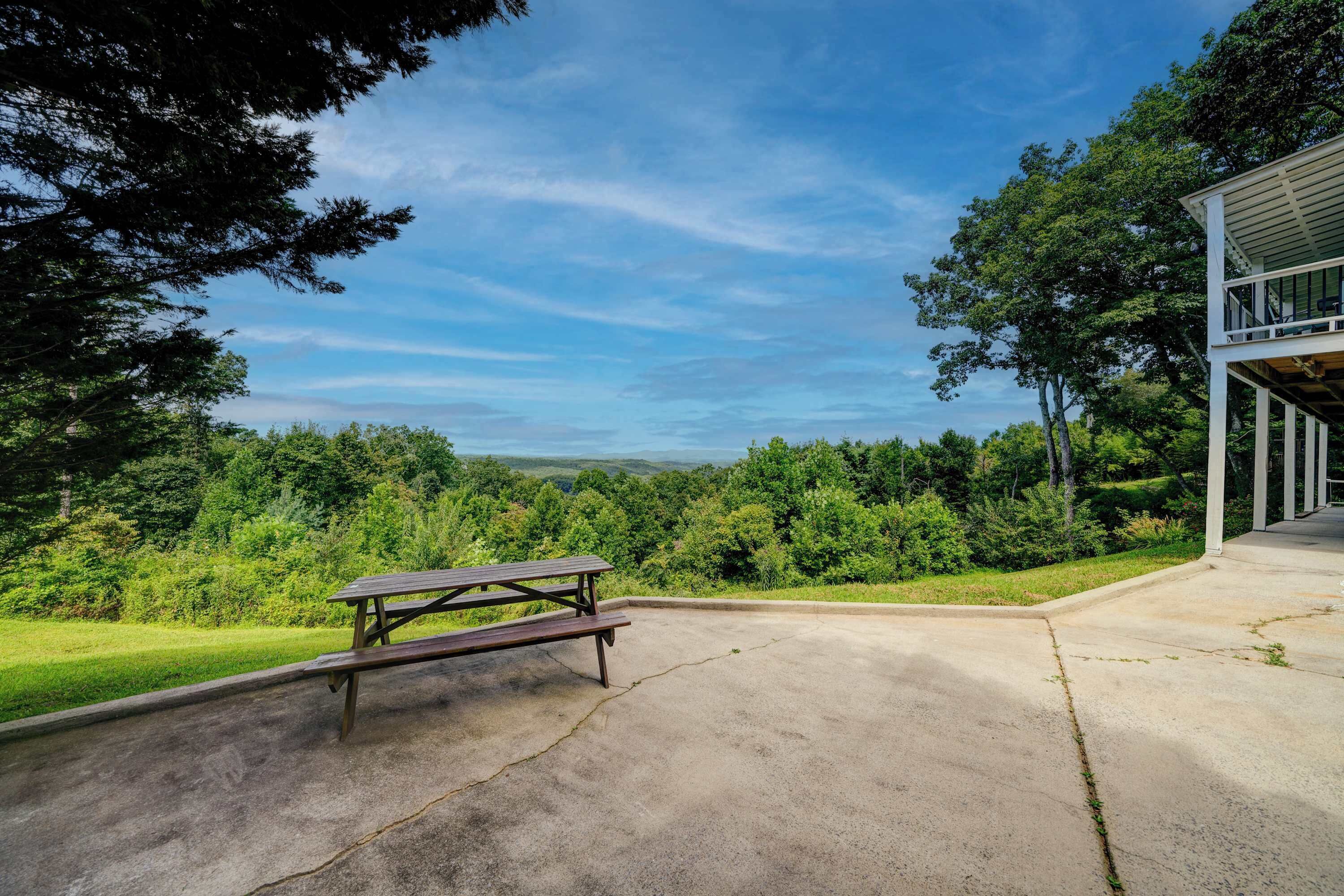 Una mesa de picnic en un área de concreto con vista a un bosque y un edificio con balcón.