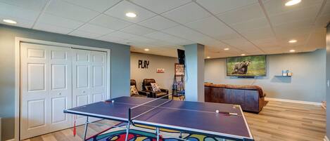 A ping pong table in a room with a colorful rug, a couch, and a wall with a bear picture.