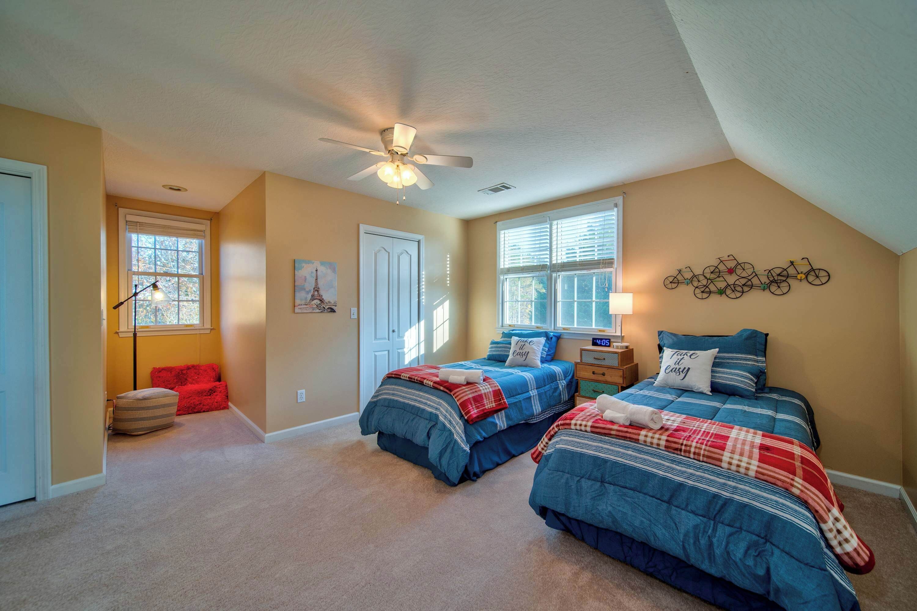 A bedroom with two beds, a ceiling fan, and a bicycle wall art piece.