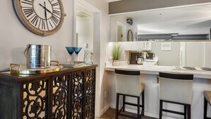 Cozinha moderna com um relógio de parede grande, área de bar com bancos e bancada com eletrodomésticos.