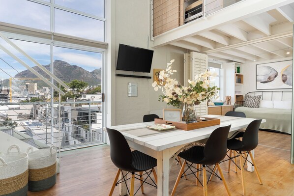 A modern dining area with a large table, chairs, and a view of the cityscape through large windows.