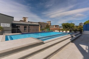 A swimming pool with steps leading into it, surrounded by a building with a sign warning about resident and visitor risk.