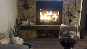 Una sala de estar con chimenea, una copa de vino tinto y una pared de piedra.