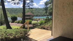 Una terraza de madera que conduce a un área de piscina con vistas a un lago y colinas.