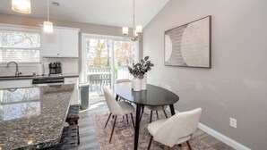 A modern kitchen with white cabinets, a granite countertop, and a dining area with a round table and chairs. - Ark Adventure Retreat (Walton)