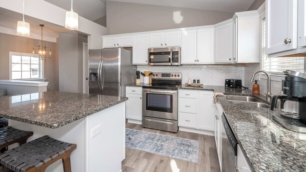 A modern kitchen with white cabinets, stainless steel appliances, granite countertops, and a built-in oven. - Ark Adventure Retreat (Walton)
