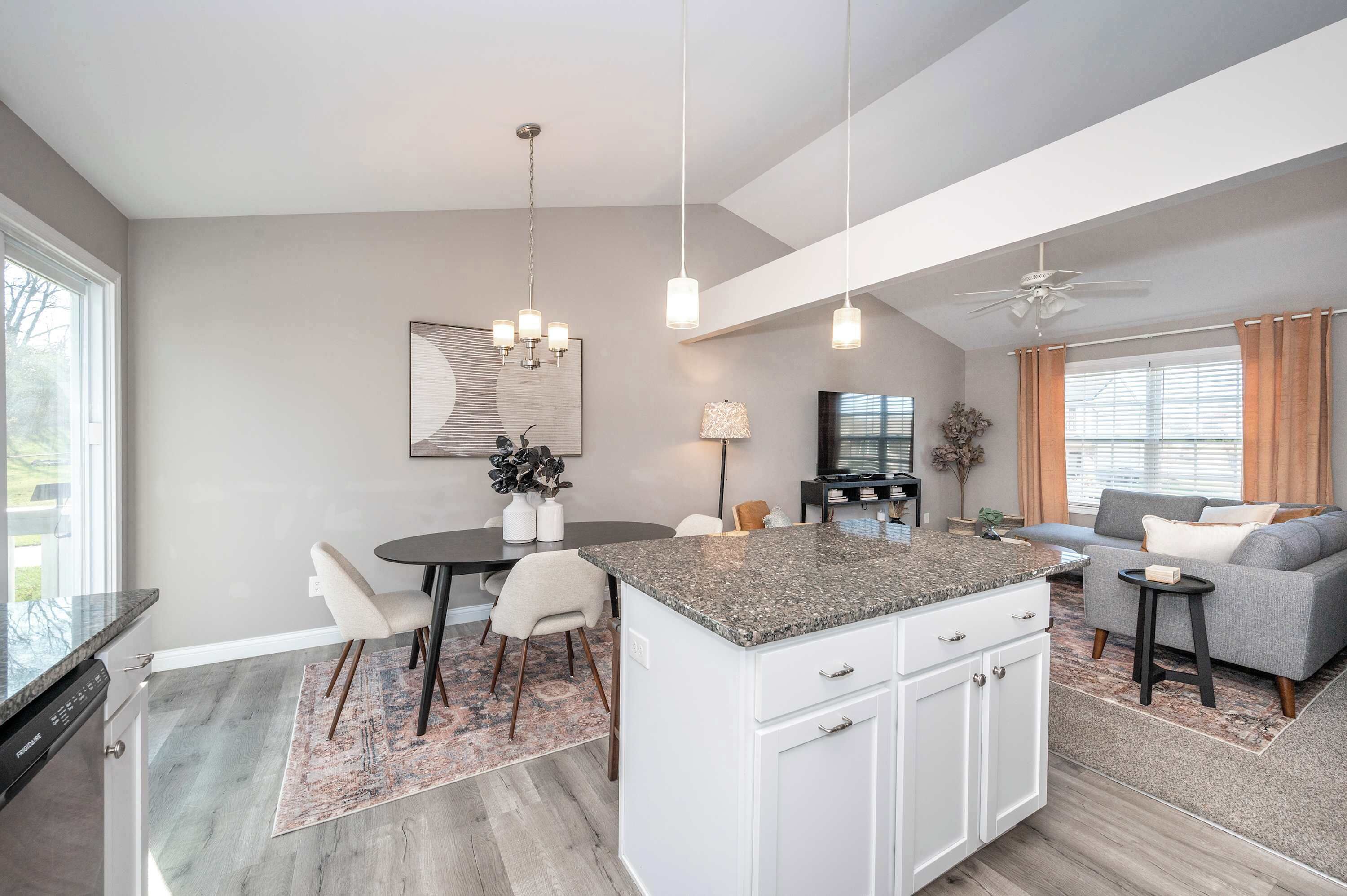 A modern kitchen with a central island, dining area, and a living space with a sofa and TV.