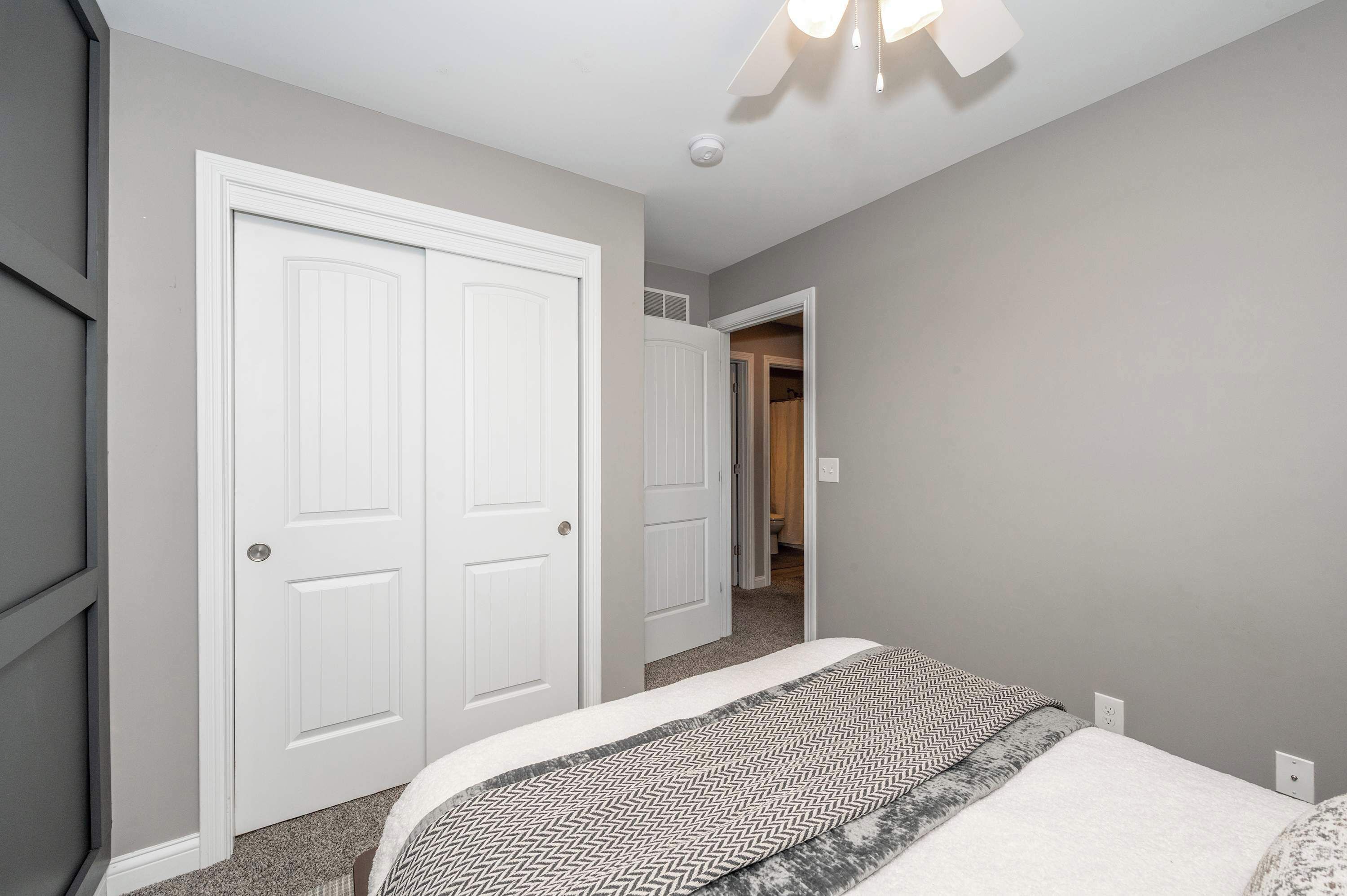 A bedroom with a bed, two white doors, and a ceiling fan.