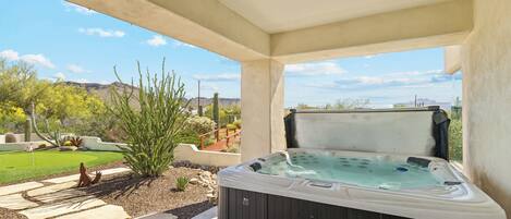 Un jacuzzi en un área exterior techada con vistas a un jardín ajardinado y montañas a lo lejos.