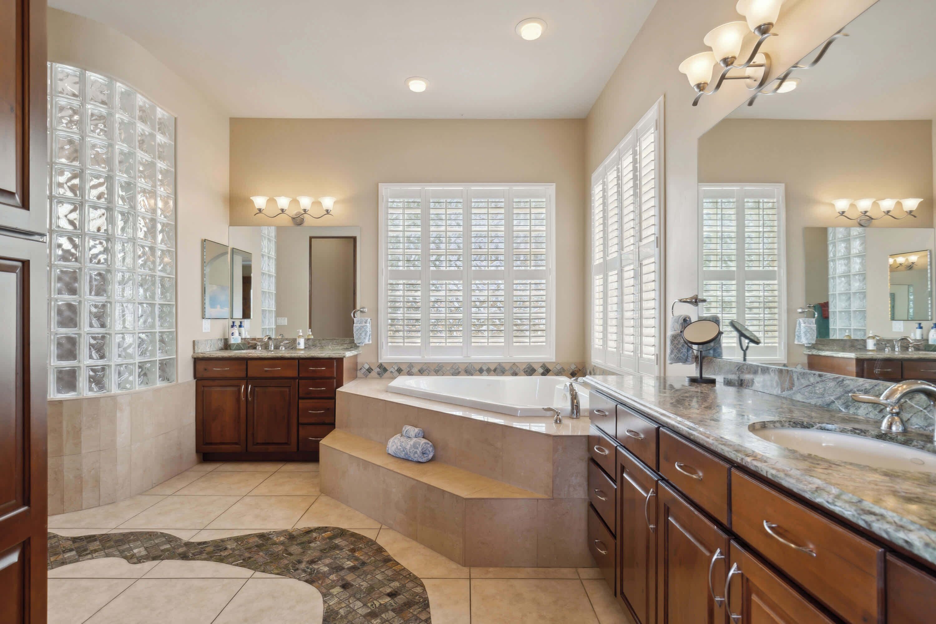 A spacious bathroom with a large bathtub, double sinks, and a vanity with a mirror.