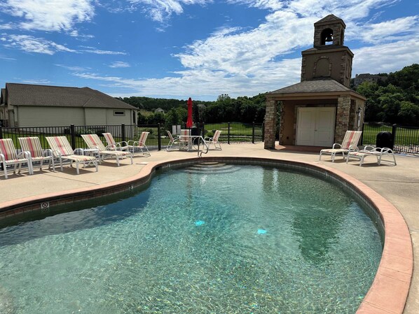 A clear swimming pool with lounge chairs and a bell tower.