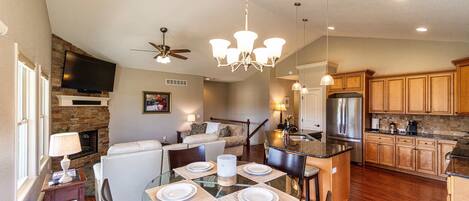 A spacious living area with a fireplace, a dining table set for four, and a kitchen with wooden cabinets and stainless steel appliances.
