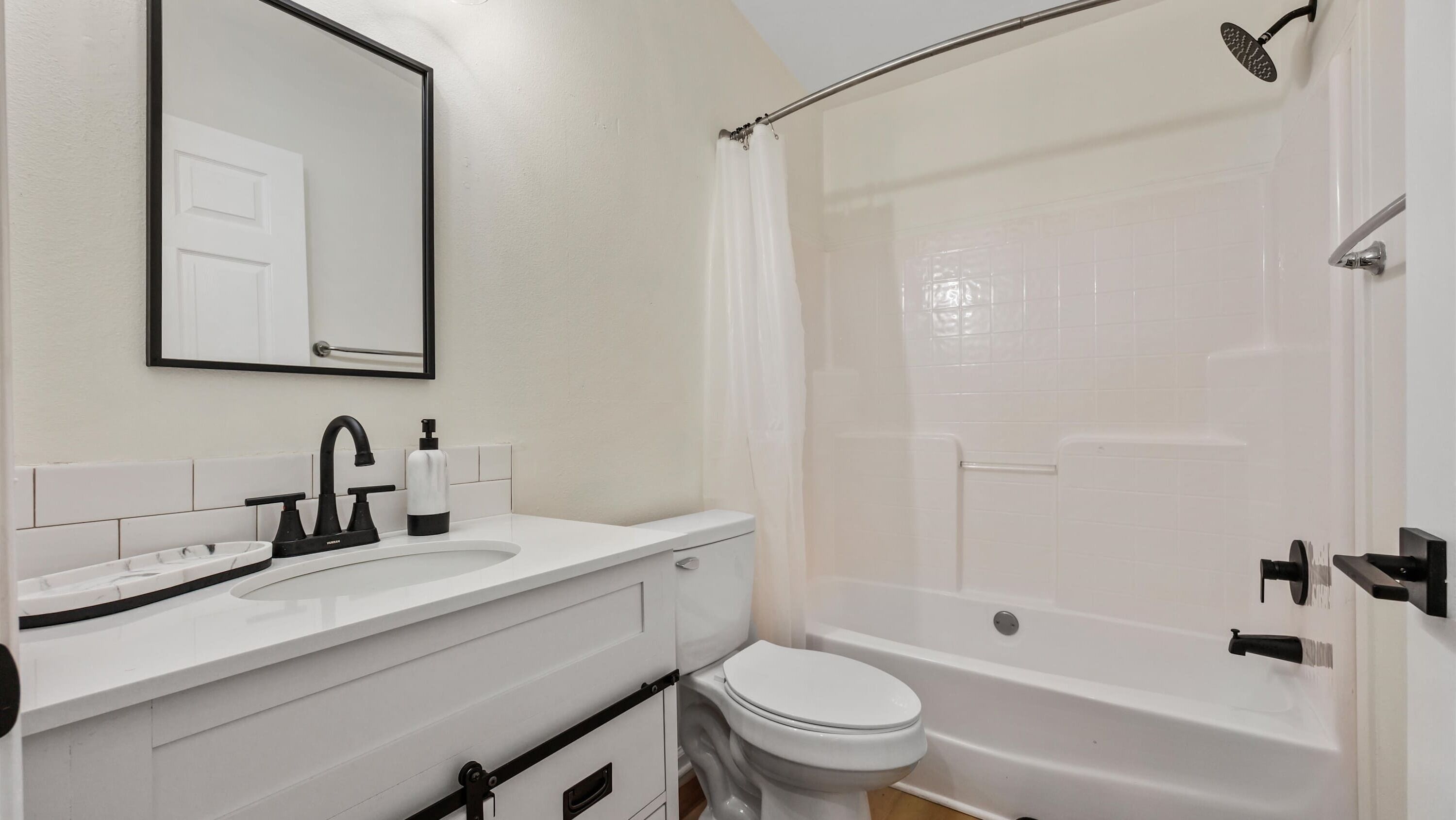 A bathroom with a white sink, black faucet, a toilet, and a shower with a curtain.