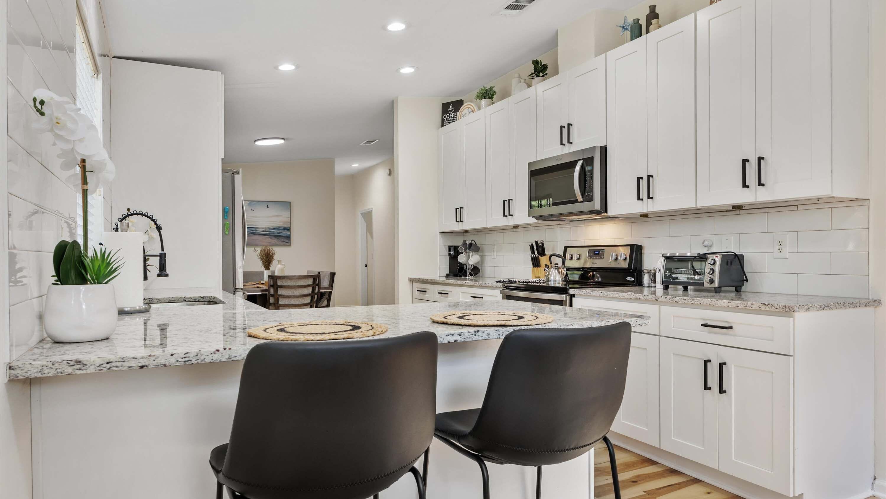 A modern kitchen with white cabinets, a granite countertop, and a dining area with two chairs.