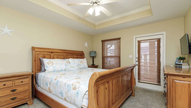 A bedroom with a wooden bed, a nightstand, a dresser, a ceiling fan, and a door with blinds. - Resort Pool! 3 Bedroom ATV Optional Sleeps 10 (Corpus Christi)