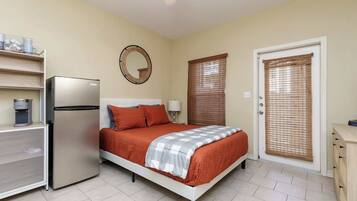 Un dormitorio con cama, refrigerador, ventana con persianas y puerta.