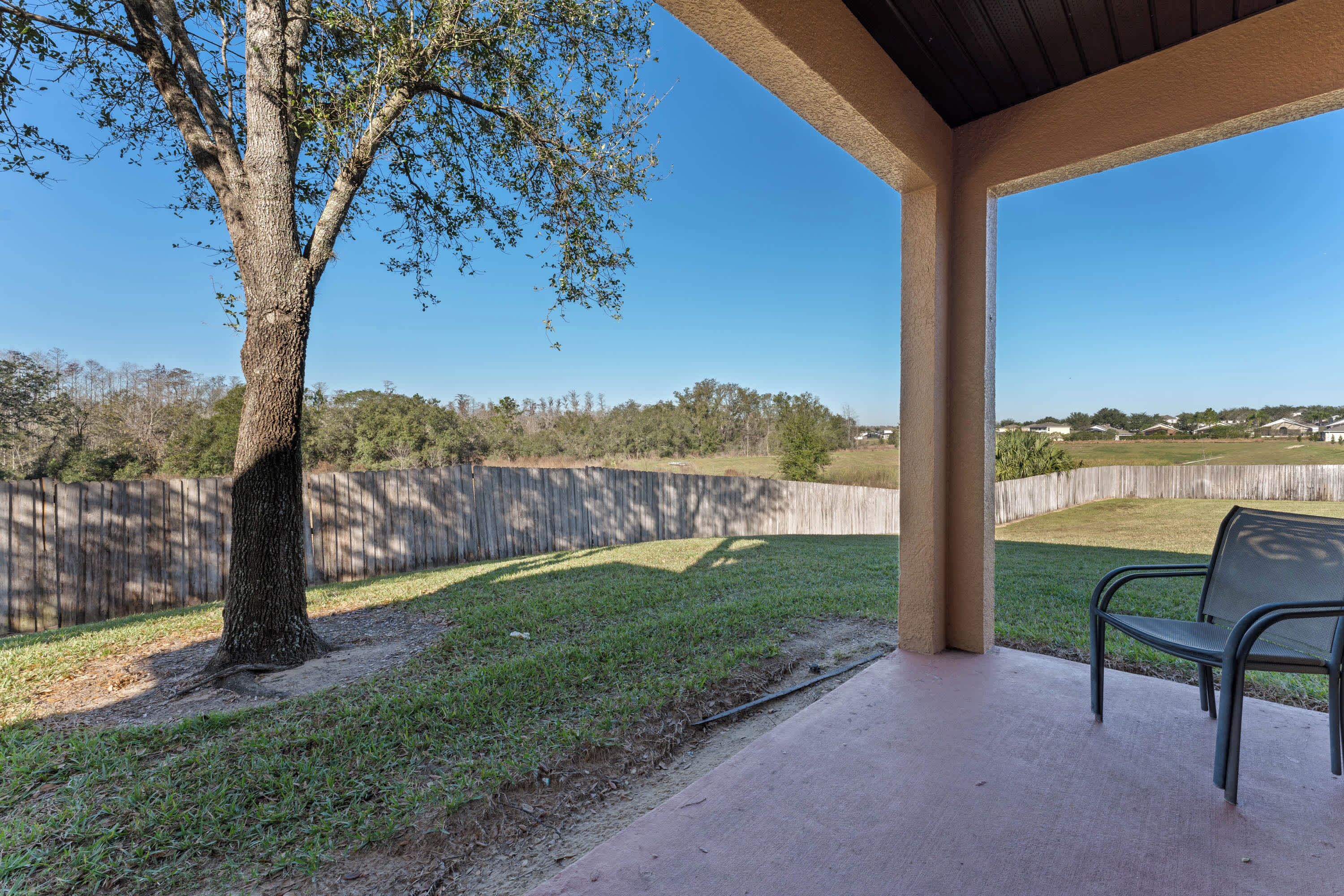 A covered patio area with a bench, a tree, and a view of a residential neighborhood.