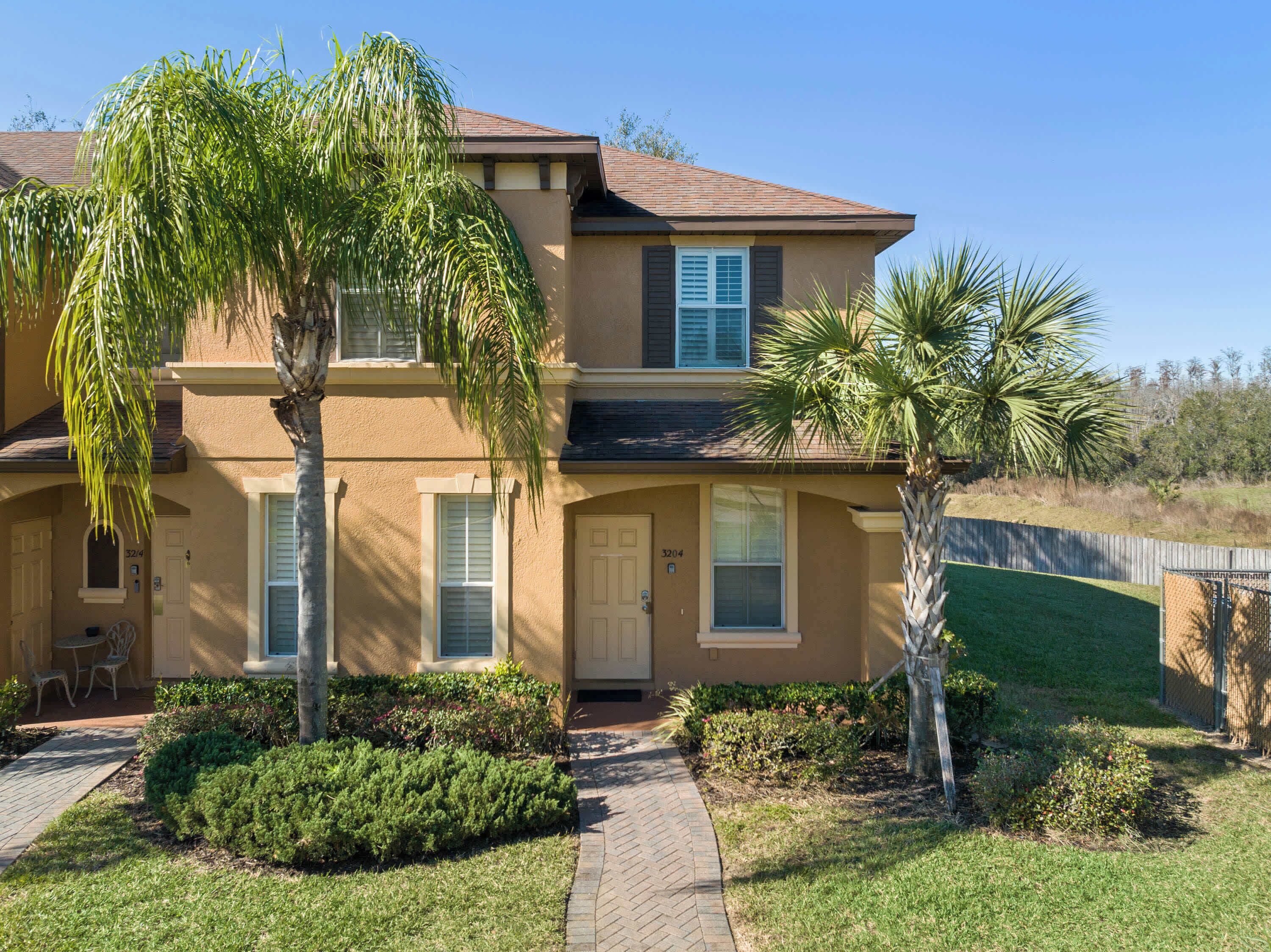 A two-story house with a beige exterior, a front porch with a bench, and a well-maintained lawn.