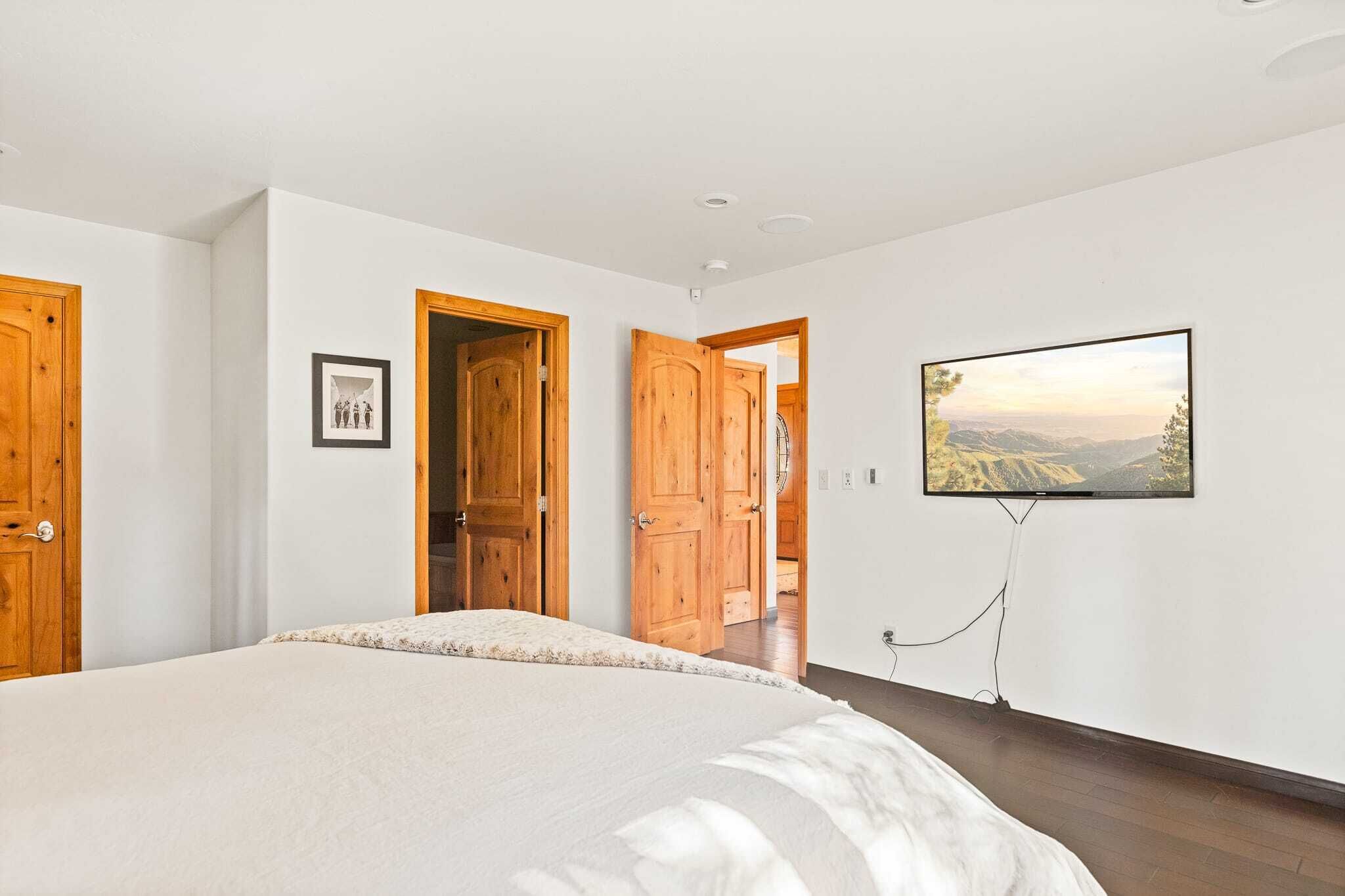 A bedroom with a large bed, wooden doors, a framed picture, and a TV mounted on the wall.