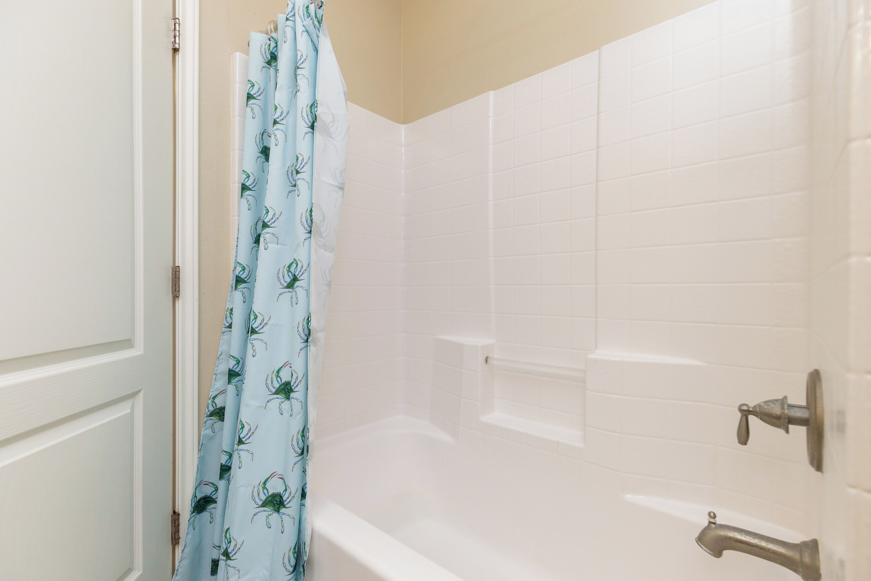 Une salle de bain avec une baignoire, des murs recouverts de carreaux blancs et un rideau de douche orné d’un motif de crabe.