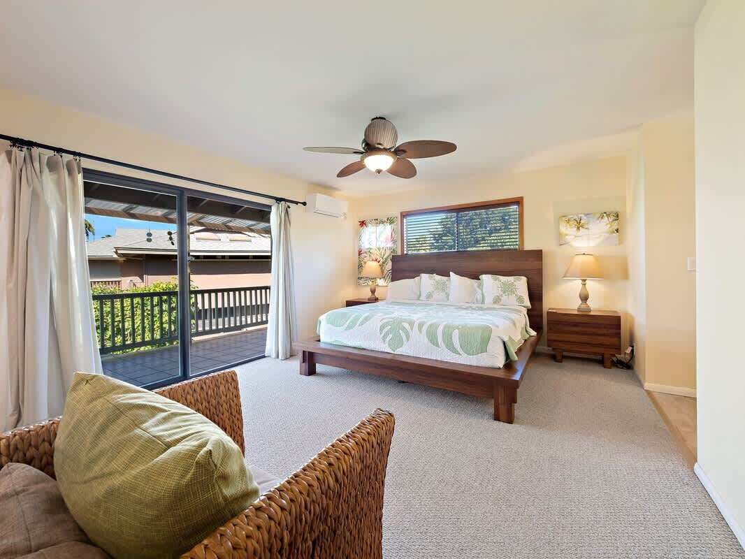 A bedroom with a bed, a ceiling fan, a nightstand, a lamp, and a view of a balcony.