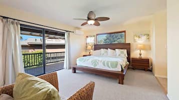 A bedroom with a bed, a ceiling fan, a nightstand, a lamp, and a view of a balcony.