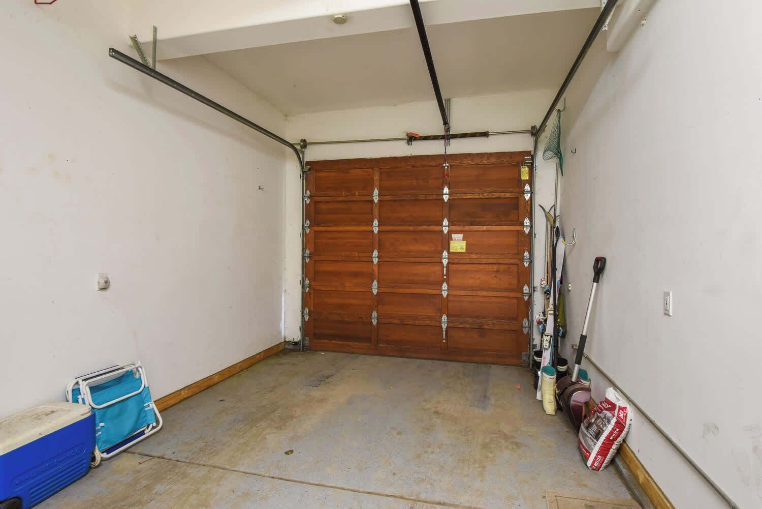 A garage with a wooden door, a blue cooler, and a broom leaning against the wall.