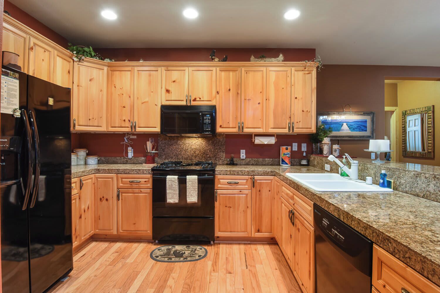 A kitchen with wooden cabinets, a black refrigerator, a microwave, a stove, and a sink.