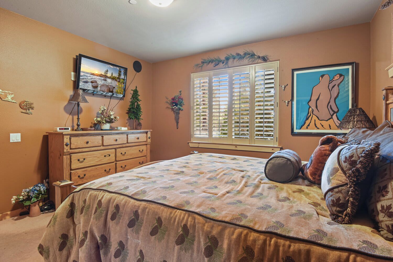 A bedroom with a bed, dresser, TV, and artwork.