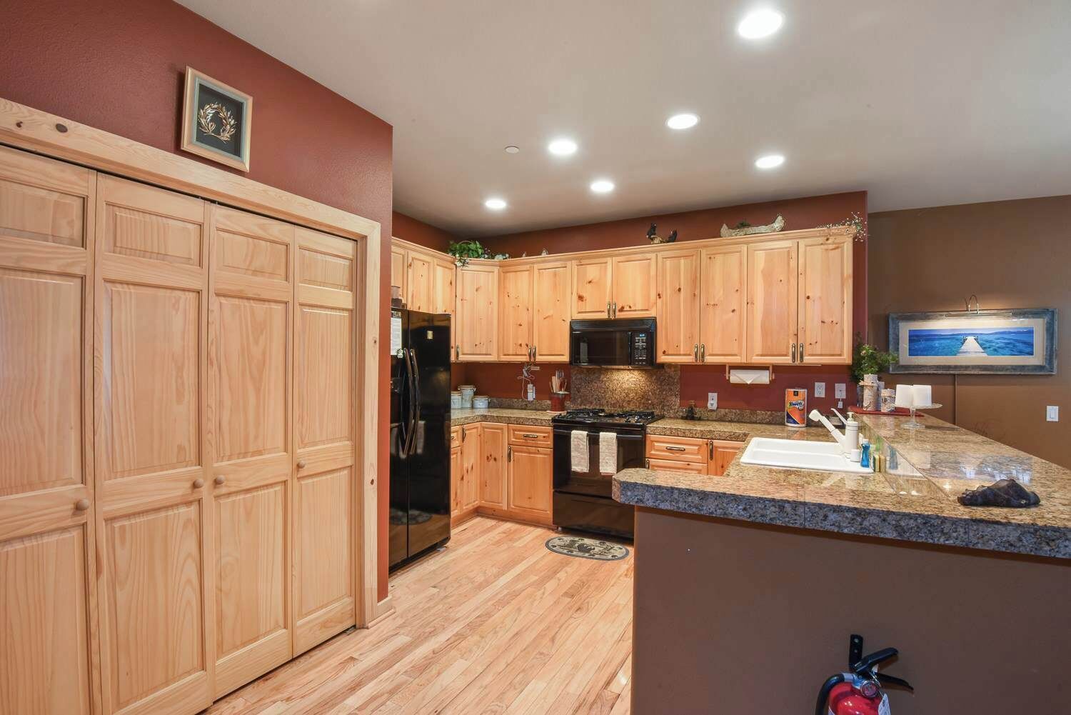 A kitchen with wooden cabinets, a refrigerator, a microwave, a stove, granite countertops, and a painting on the wall.