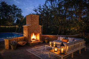 An outdoor patio with a brick fireplace, a pool, and a seating area with cushions and lanterns. - POOL+HOT TUB, 2 KING BEDS, OUTDOOR FIRE/OASIS, PLAYGROUND, THEATER, WORKOUT ROOM (Columbus)