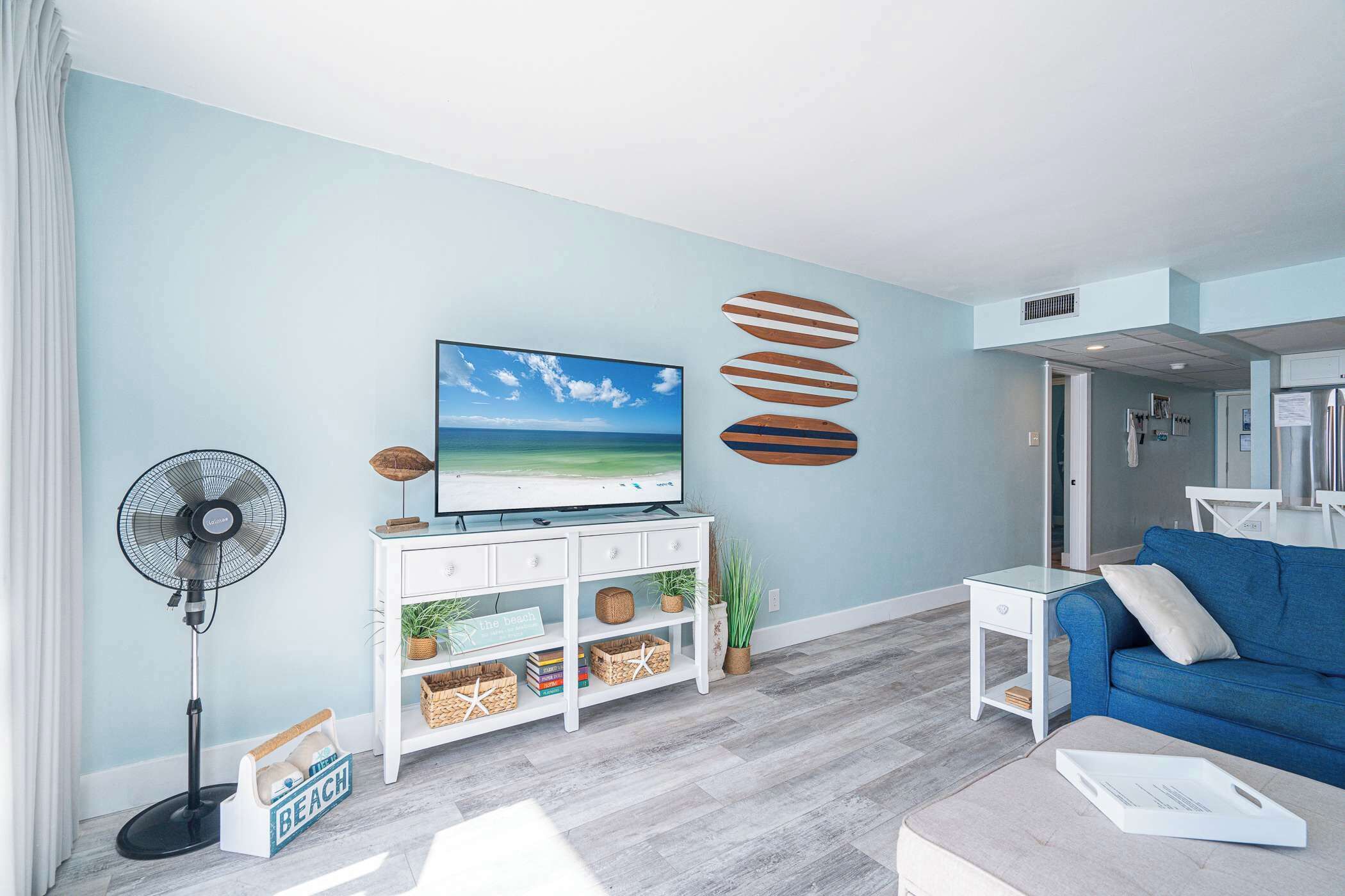 A living room with a TV, a fan, a blue sofa, and a white coffee table.