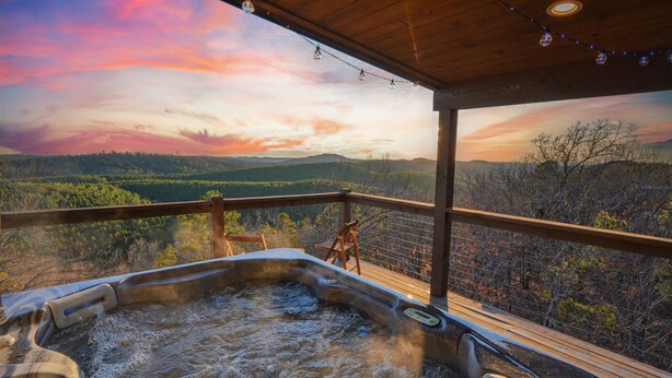 Ein Whirlpool auf einer Holzterrasse mit Panoramablick auf Berge und Bäume.