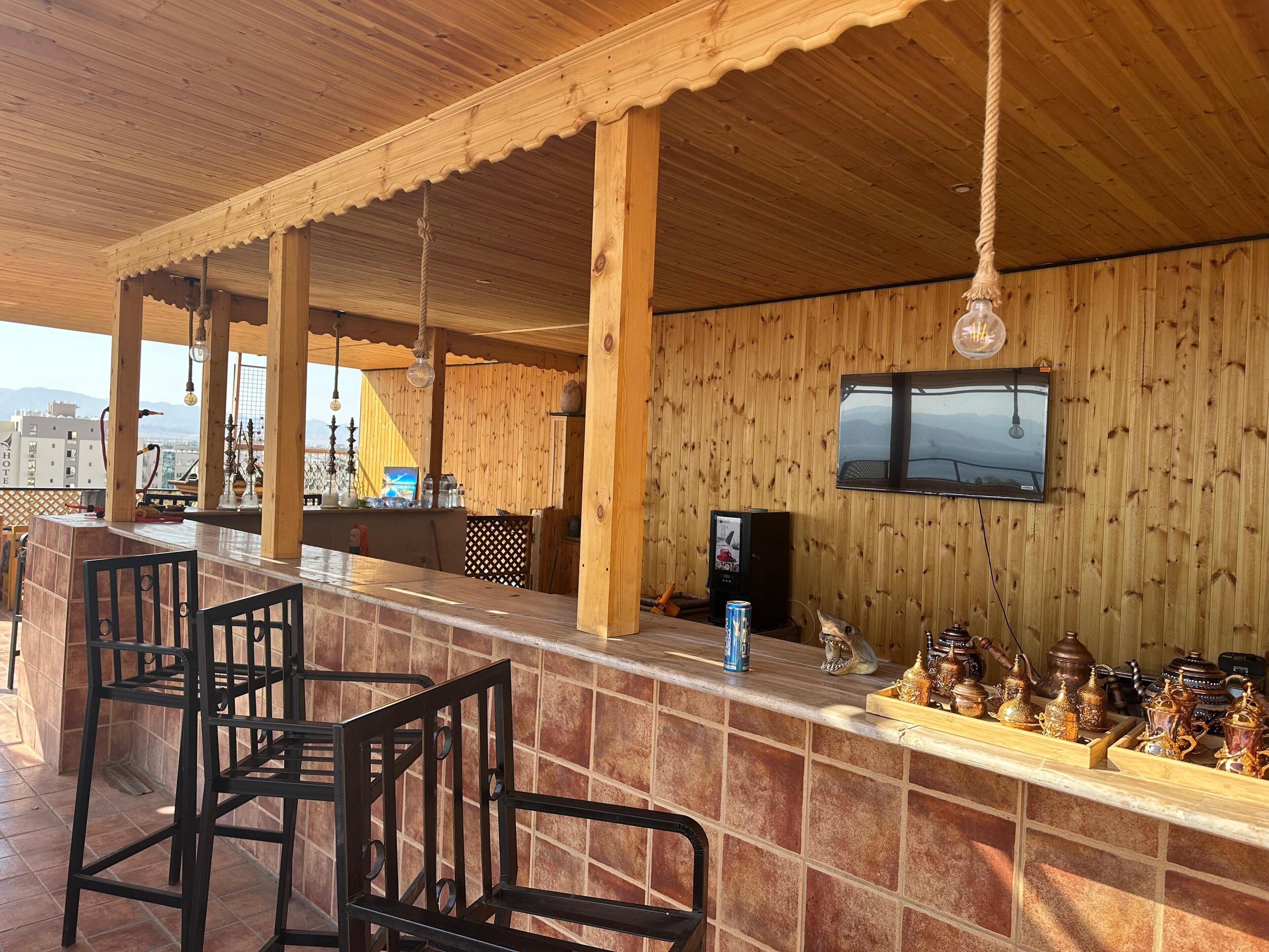 A wooden bar area with a television, bar stools, and a variety of decorative items on the counter.