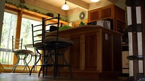 Un interno in legno con angolo cottura, che include uno sgabello da bar, mobili in legno e una finestra con vista sugli alberi.