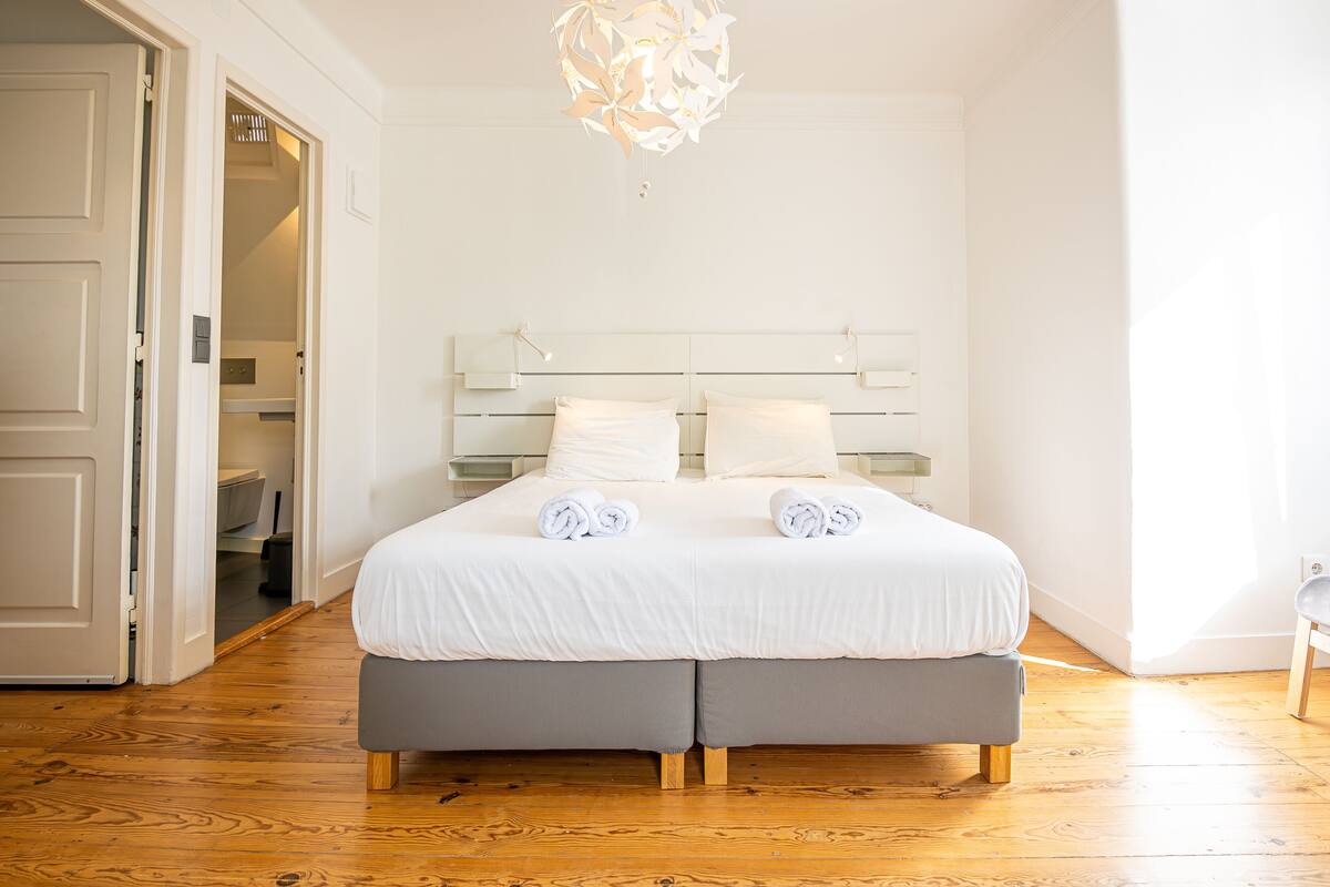 A bedroom with a double bed, grey upholstered headboard, white bedding, and a modern chandelier.
